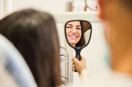 Ασθενής κοιτάει το χαμόγελο της σε καθρέπτη στο οδοντιατρείο του Μπέρτου Λουίτζι